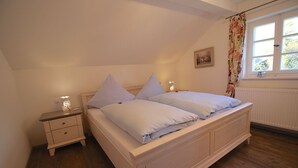 A bedroom with a single bed, a nightstand, a window with curtains, and a radiator. - Alpenschloss (Garmisch-Partenkirchen)