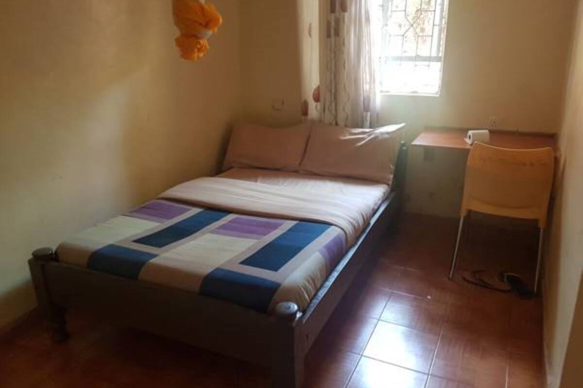 Una cama individual con colcha, una silla, una mesita y una ventana con cortinas.