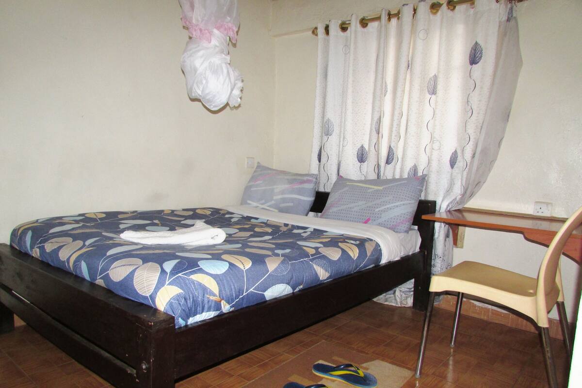 Una cama individual con una colcha estampada, una mesita de noche, una silla y un perchero.