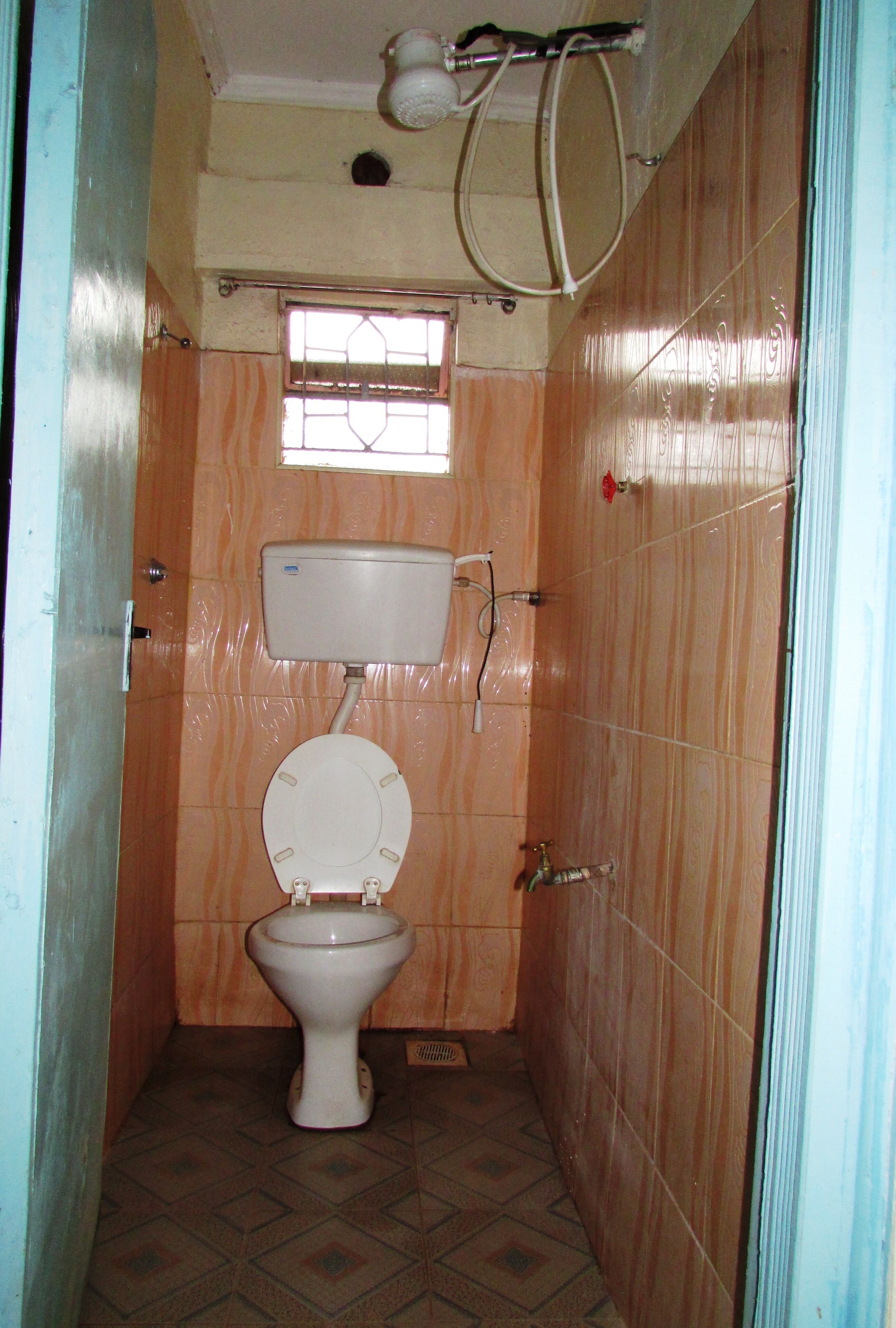 A small, narrow bathroom with a toilet, a window, and a shower area.
