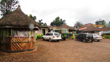 A rural setting with thatched-roof huts, a gravel road, and parked cars.
