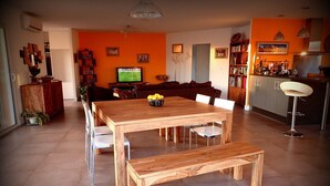 A modern living room with a wooden dining table and benches, a television, and a kitchen area with a bar. - NEW Villa with JACUZZI, near St Cyprien beach (LECCI)