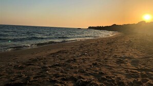 Une plage, un ciel dégagé et le soleil qui se couche à l’horizon.