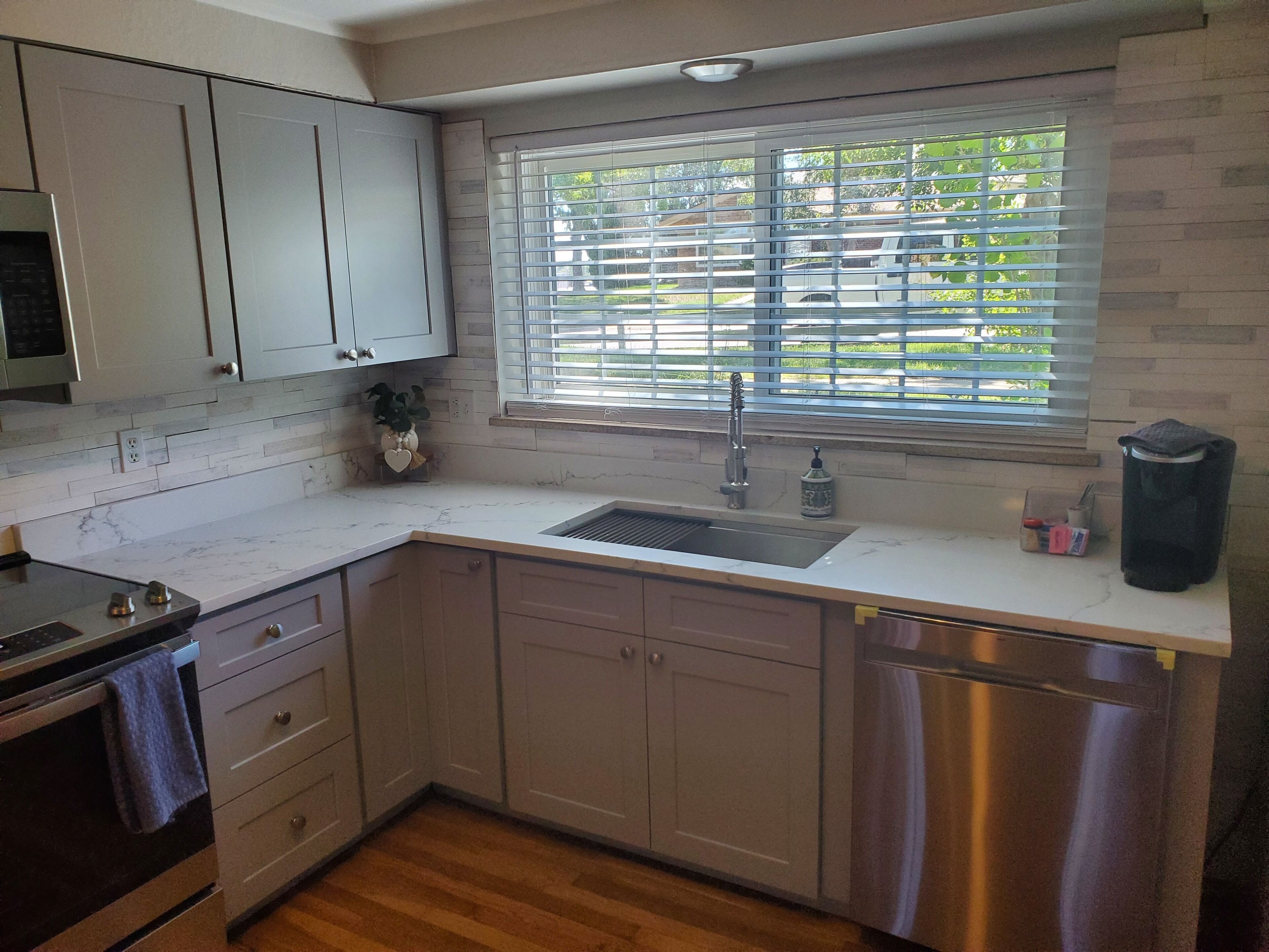 A kitchen with a sink, stove, cabinets, and a window with blinds.