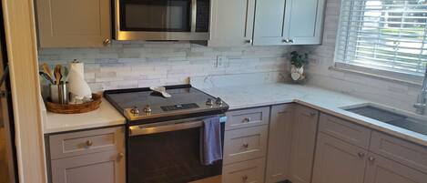 A modern kitchen with stainless steel appliances, light grey cabinets, and a wooden floor.