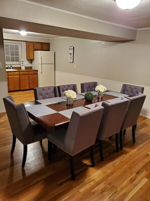 A dining room with a wooden table, eight upholstered chairs, and a kitchen in the background.