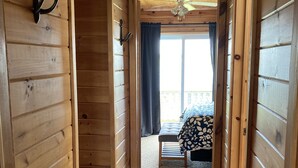 A wooden interior hallway leading to a bedroom with a bed and a window. - Riverview Cottage on Green Gables Shore (Anglo-Rustico)