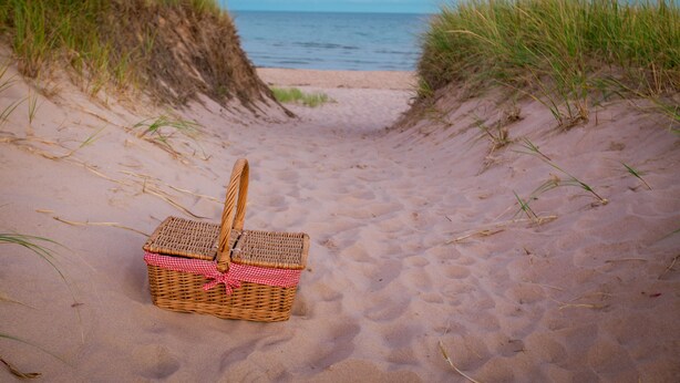 A beach scene with a wicker picnic basket on the sand. - Riverview Cottage on Green Gables Shore (Anglo-Rustico)