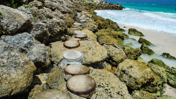 Eine felsige Küstenlinie mit großen Felsen und einer Reihe flacher Steine, die zum Strand führen.