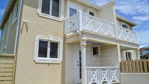 Ein zweistöckiges Gebäude mit Balkon, Holzzaun und sandfarbenem Putz.