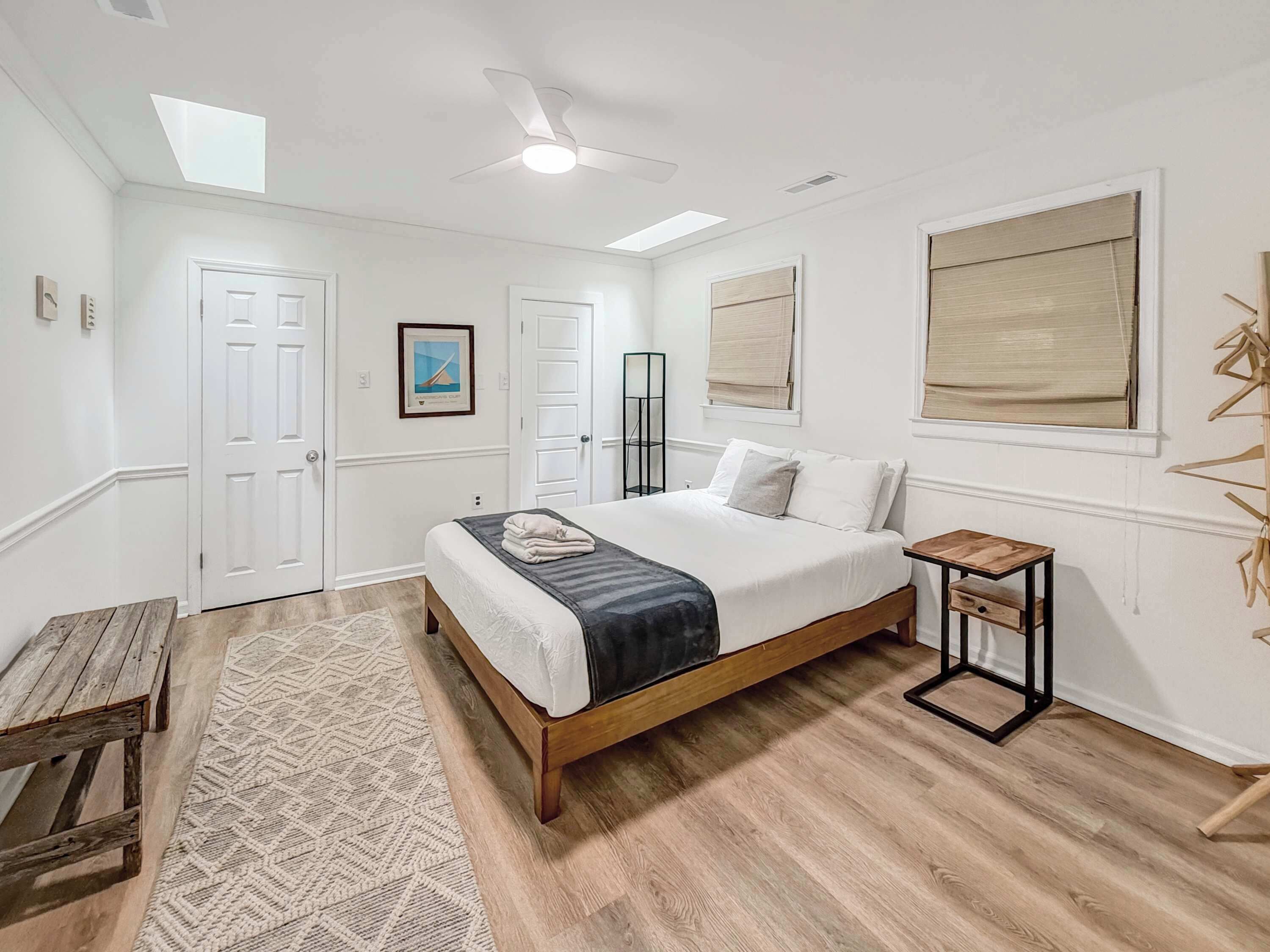 A bedroom with a bed, a ceiling fan, a wooden bench, a patterned rug, and a painting on the wall.