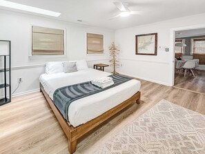Ein Schlafzimmer mit einem Bett, einer Stehlampe, einer Karte an der Wand und einem Essbereich, der durch eine offene Tür sichtbar ist.