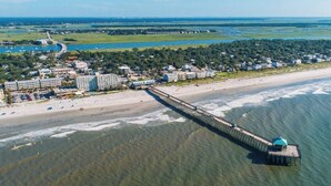 An aerial view of a coastal area with a long pier extending into the water, surrounded by buildings and a beach.