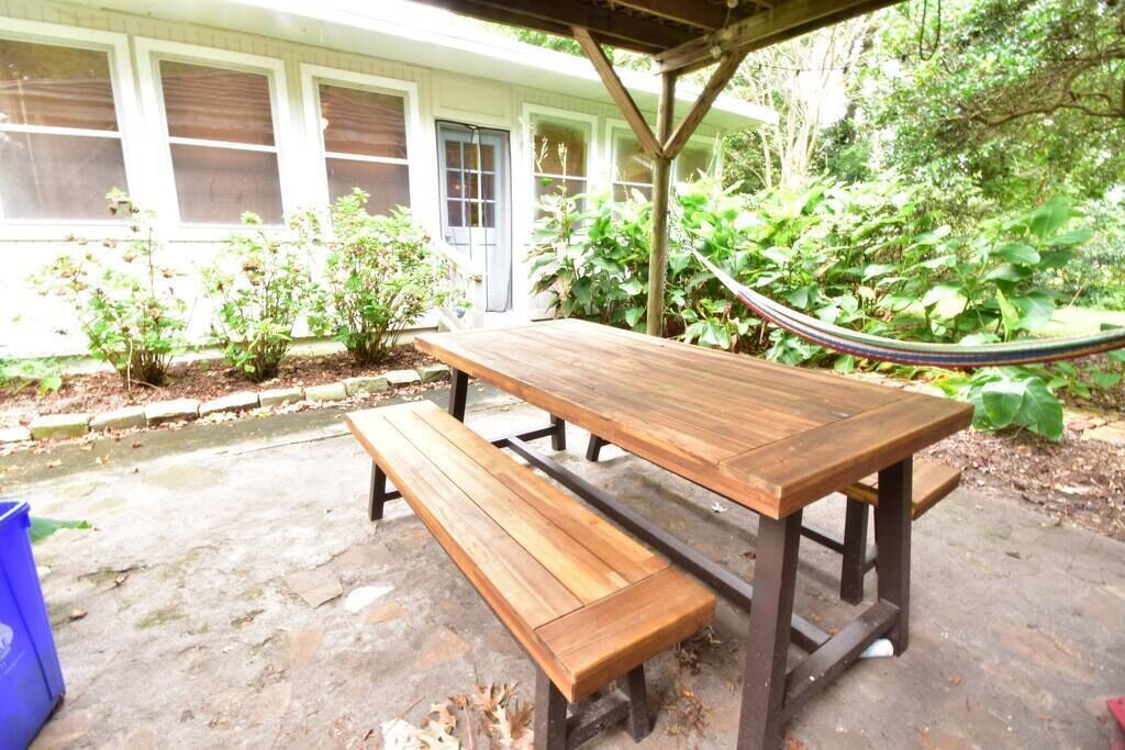 An outdoor wooden picnic table with benches, surrounded by greenery and a hammock.