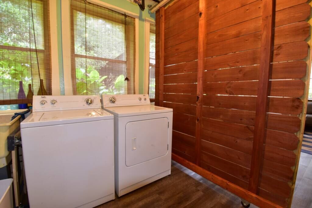 Une buanderie équipée de deux machines à laver, avec une porte en bois et des fenêtres dotées de stores.