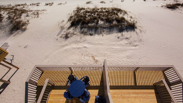 Uitzicht op het strand vanaf een houten terras met een ronde tafel en stoelen.