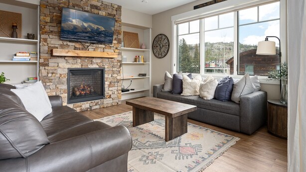 A living room with a stone fireplace, a sofa, a coffee table, and a large window with a view of the outdoors.