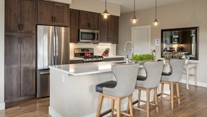 A modern kitchen with dark wood cabinets, stainless steel appliances, a central island with bar stools, and pendant lighting.