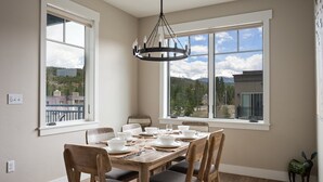 A dining room with a wooden table set for six, large windows with a view of mountains, and a chandelier.