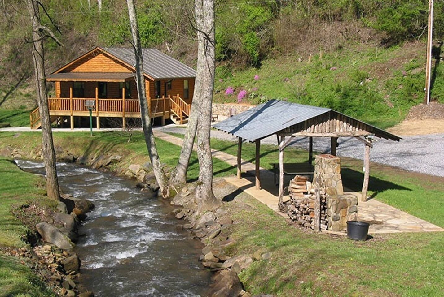 Uma pousada com uma cabana de madeira e um pavilhão coberto à beira de um riacho.