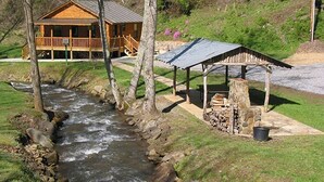 Una cabaña de madera junto a un arroyo, con un pabellón cubierto.