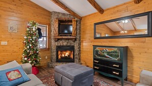 Interior acogedor de una cabaña de madera con chimenea de piedra, un televisor y un árbol de Navidad.