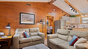 Interior acogedor de una cabaña con paredes de madera, un cuadro enmarcado, una kitchenette y dos sofás con cojines.
