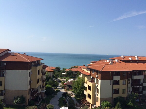 A residential area with apartment buildings, a central pathway, and a view of the sea.
