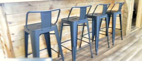 A row of three blue bar stools against a wooden wall with a kitchen counter above.
