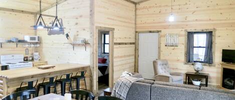 L’intérieur chaleureux d’un chalet avec une table à manger en bois, des chaises, un canapé, un téléviseur et un ventilateur de plafond.