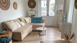 A modern living room with a beige sectional sofa, a small round coffee table, and a wooden chair. - Charming renovated luxury apartment with seaview. (De Haan)