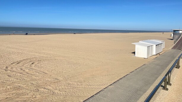 A beach with a concrete walkway, a lifeguard tower, and white beach huts. - Charming renovated luxury apartment with seaview. (De Haan)