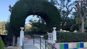 Un camí que travessa un jardí amb un gran arc, parets de pedra i una zona de jocs colorida.