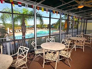 Eine Terrassengaststätte mit runden Tischen und Korbstühlen mit Blick auf einen Pool und Palmen.