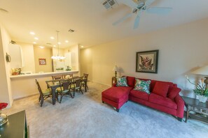A living room with a red sofa, a dining table with chairs, a ceiling fan, and a framed picture on the wall.