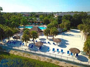 A resort with a pool, beach chairs, umbrellas, and palm trees.