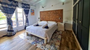 Un dormitorio con cama, mesitas de noche, cabecera de ladrillo y suelo con diseño. Se ve un paisaje a través de una puerta.