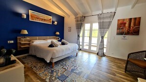 Un dormitorio con cama, mesita de noche, lámpara, un cuadro y vistas al exterior a través de una puerta.