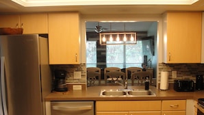 A modern kitchen with a stainless steel refrigerator, a dishwasher, a double sink, and wooden cabinets. - Sandy Shores Villa near Sieta Key and other beaches (Sarasota)