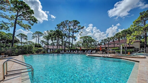 A clear swimming pool with lounge chairs and umbrellas, surrounded by trees and buildings. - Sandy Shores Villa near Sieta Key and other beaches (Sarasota)