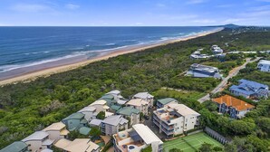 An aerial view of a coastal residential area with houses, a beach, and a tennis court. - Castaway Cove Castaways Beach (Castaways Beach)