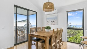 A dining area with a wooden table and chairs, a hanging light fixture, and a large window with a view of the sea. - Castaway Cove Castaways Beach (Castaways Beach)