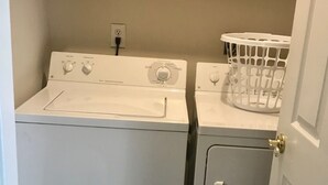 Une buanderie équipée de deux machines à laver et d’un sèche-linge, d’un panier à linge blanc et d’une porte dotée d’une poignée en laiton.