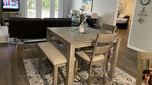 Un coin repas avec une table et des chaises en bois, un lustre et un téléviseur en arrière-plan.