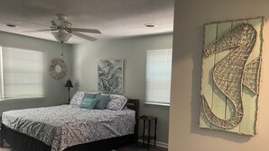 Une chambre à coucher avec un lit, un ventilateur de plafond, une œuvre d’art murale et une fenêtre avec des stores.