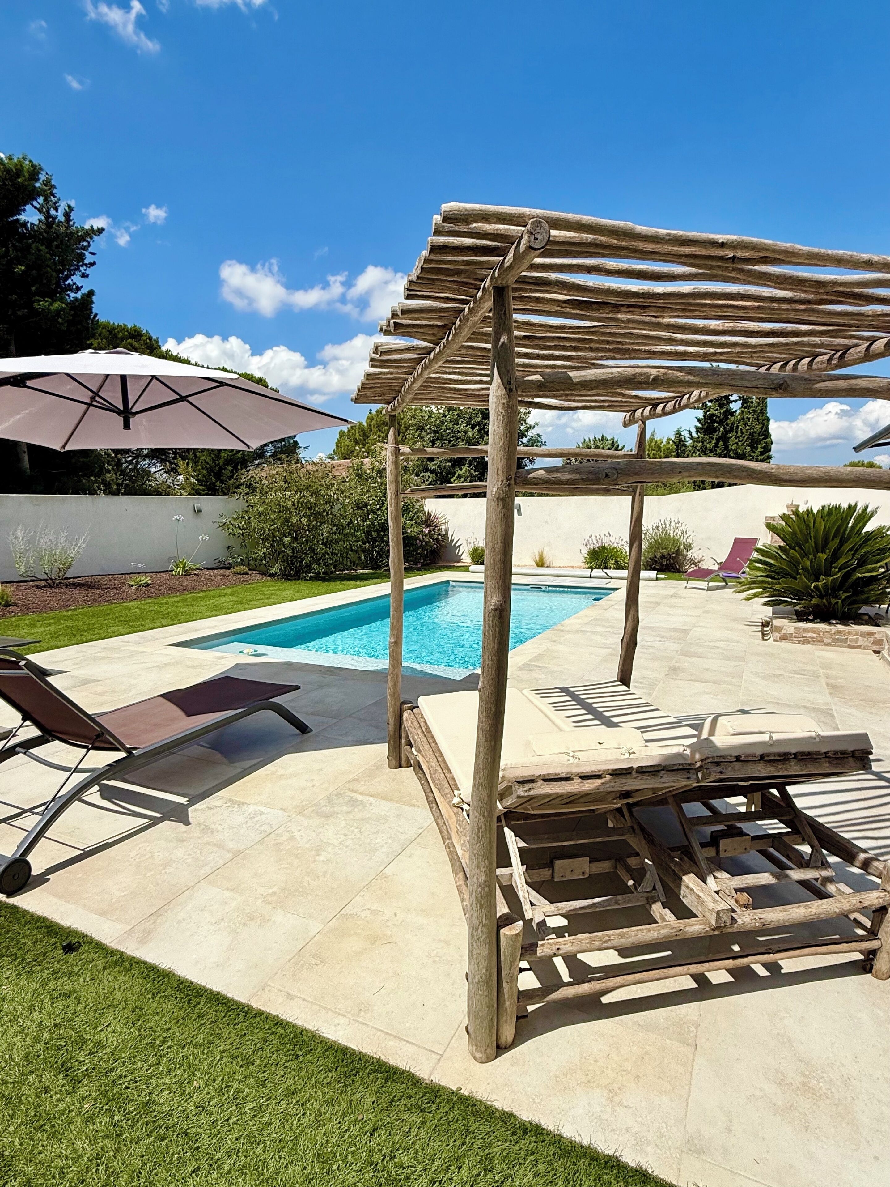 Un jardin avec une piscine, une pergola en bois et des chaises longues.
