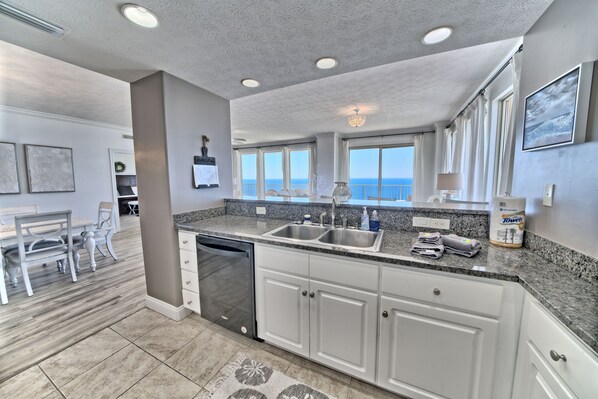 A modern kitchen with granite countertops, white cabinetry, and a dishwasher. There are large windows offering a view of the ocean. - Beautiful 3 bedroomTreasure IslandViews from every room,hot tub,wraparound deck. (Panama City Beach)
