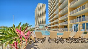 A hotel pool area with lounge chairs and a tall building in the background.