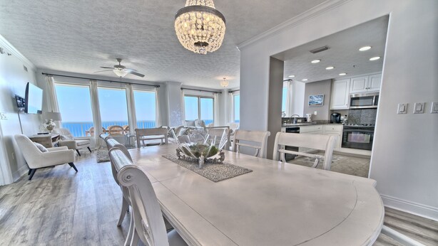 A spacious dining area with a large island, white furniture, and a chandelier.