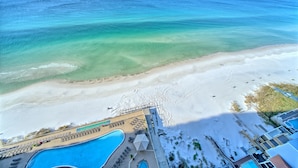 A beach resort with a swimming pool, beach chairs, umbrellas, and a view of the ocean.